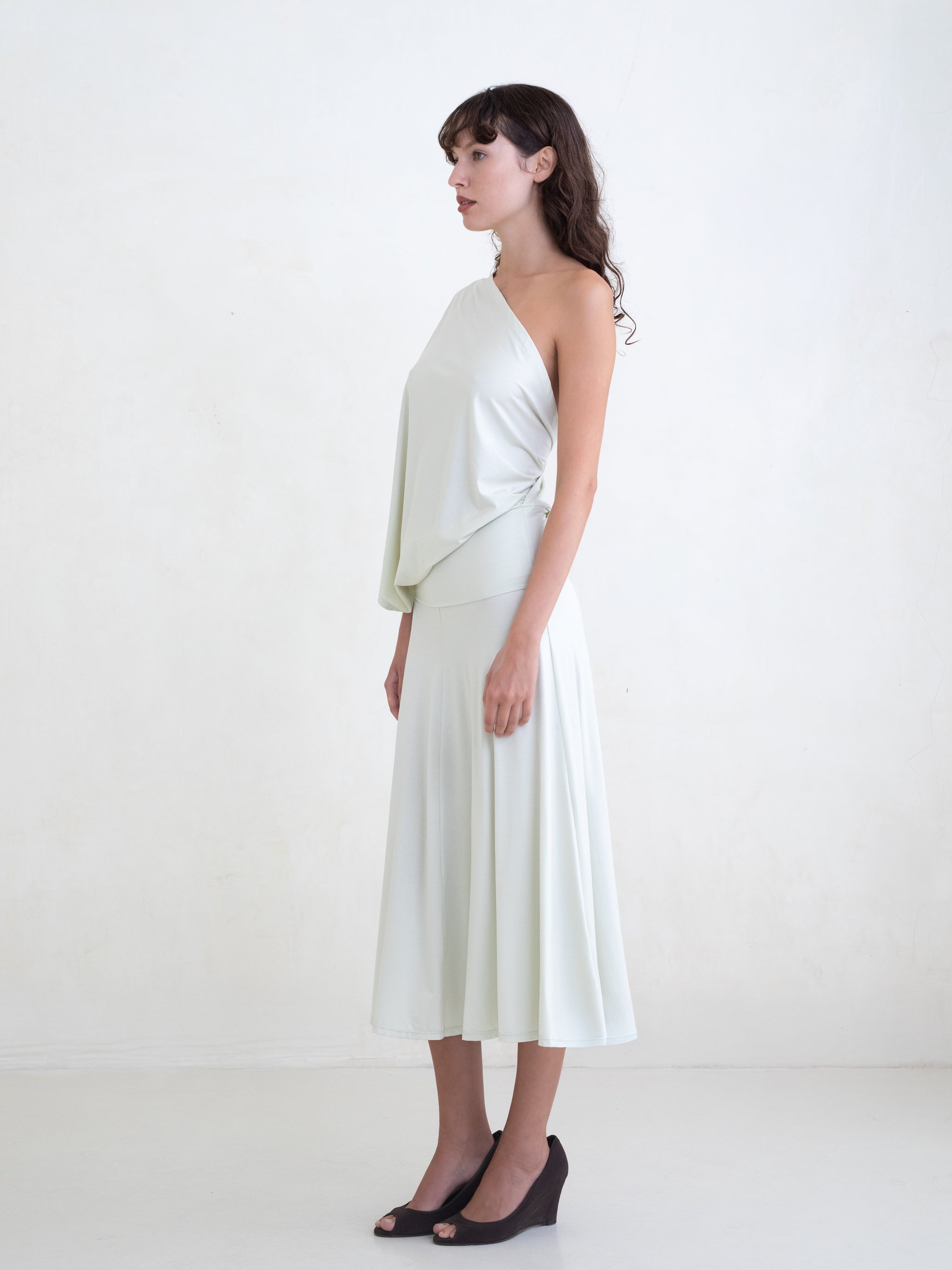 Woman wearing a light green one-shoulder midi dress on a white background 