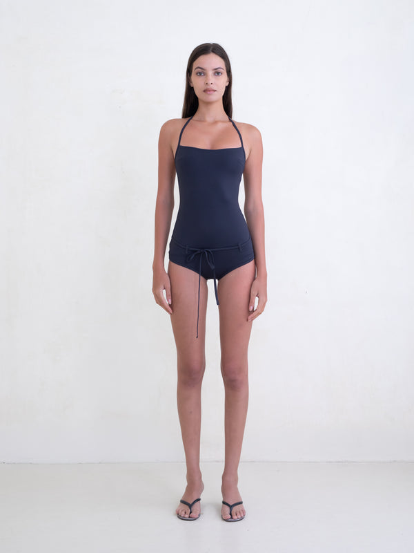 Woman wearing a navy one-piece swimsuit on a white background. 
