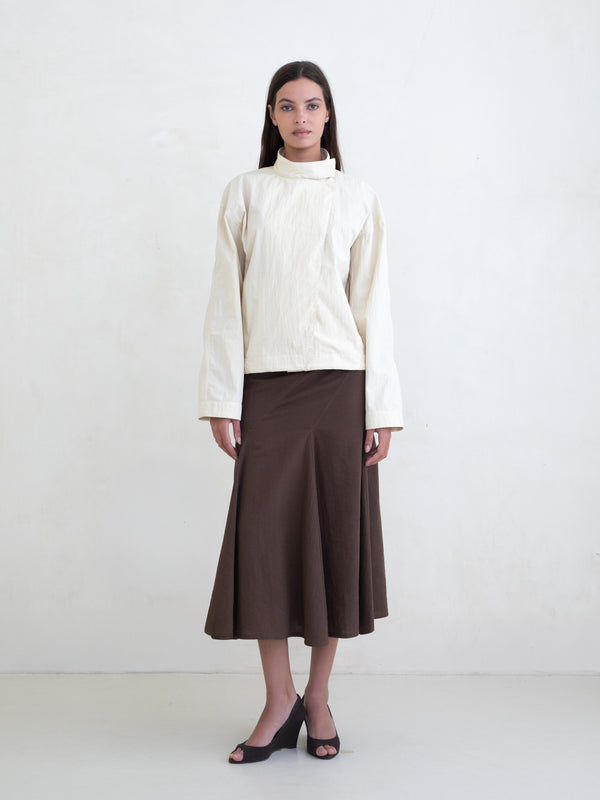 Woman wearing a cream jacket and a brown midi skirt on a white background. 