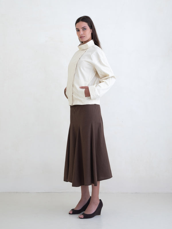 Woman wearing a cream jacket and a brown midi skirt on a white background. 