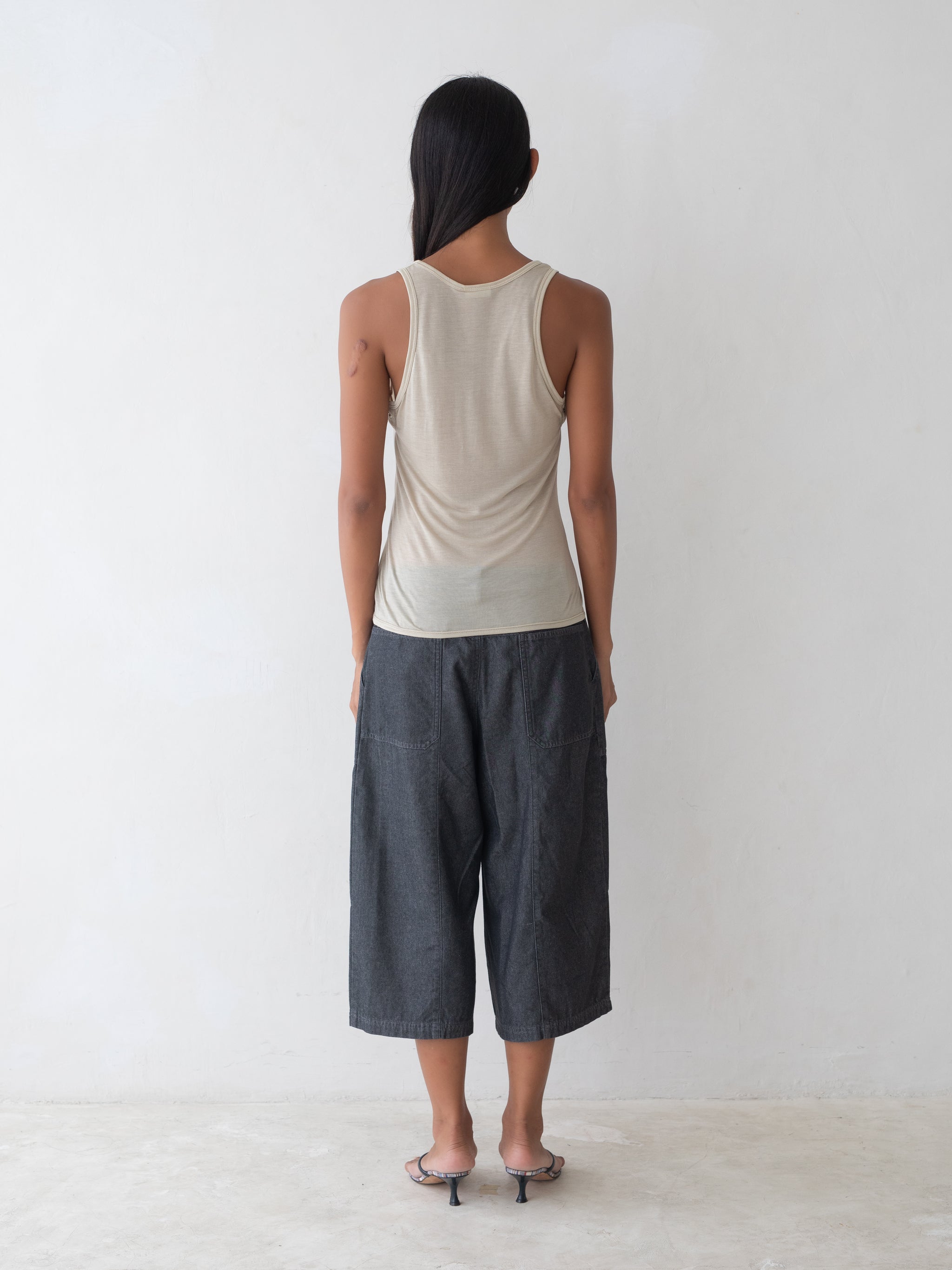 Woman wearing a beige tank top and dark gray pants on a white background